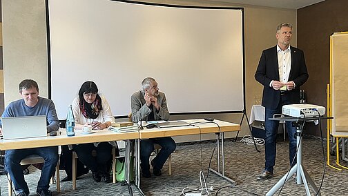 Der Redner steht vor einer Leinwand